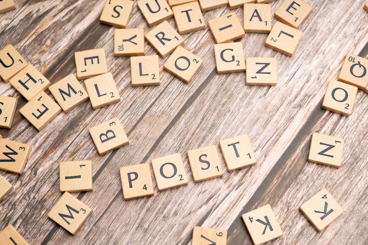 gallery-6 Wooden scrabble tiles scattered with the word 'POST' on a rustic wooden surface.