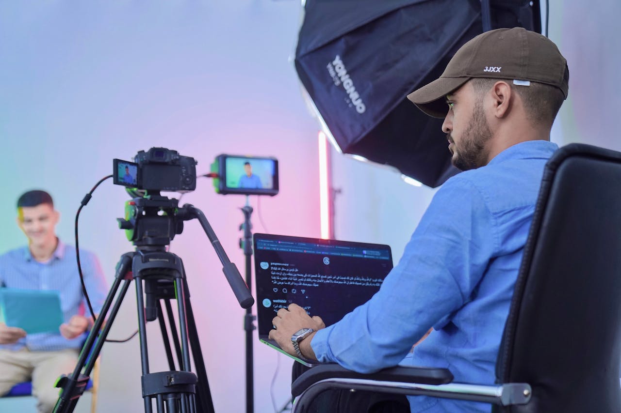 gallery-2 Man operates camera and laptop during a studio video shoot with a host and camera crew.