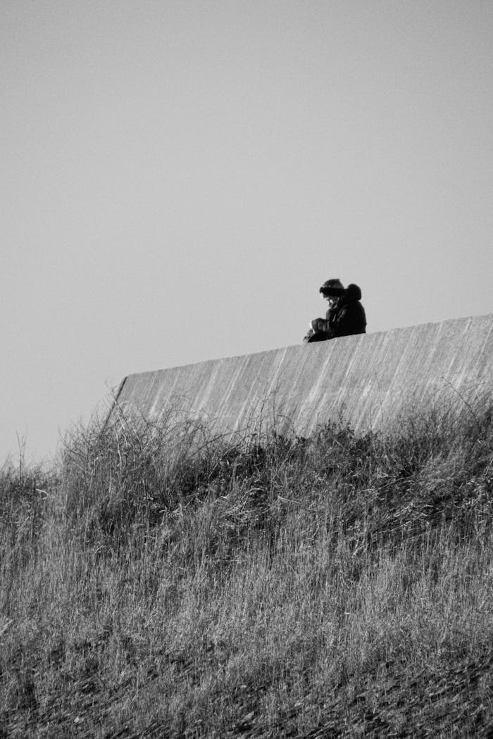 services-02 Black and white photo of a person sitting alone on a wall, contemplating in solitude.