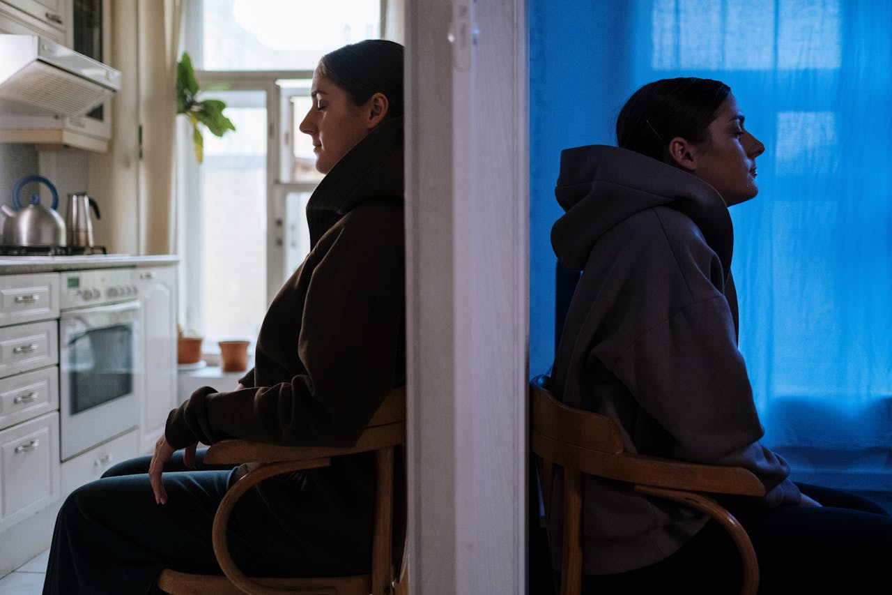 about-01 Two women sitting back to back, embodying contrasting emotions in a split room.